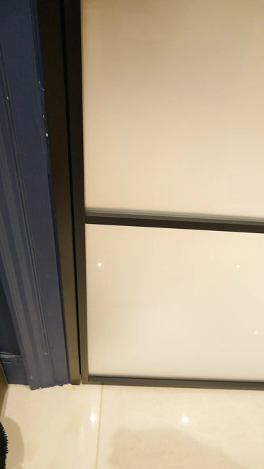 Close-up of hinged frosted glass door framed in black metal, adjacent to blue doorframe and tiled floor