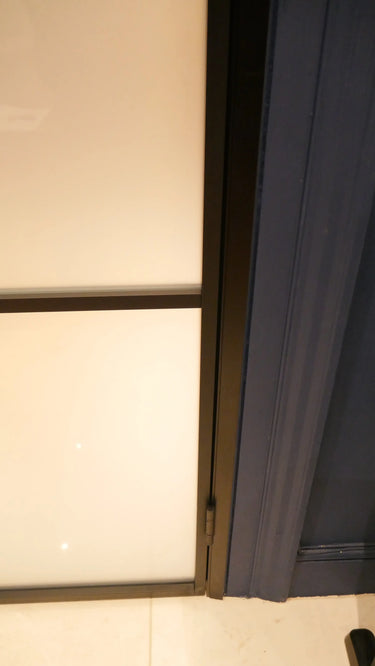 Close-up of a hinged frosted glass door with dark metal frame and blue door trim on tiled floor