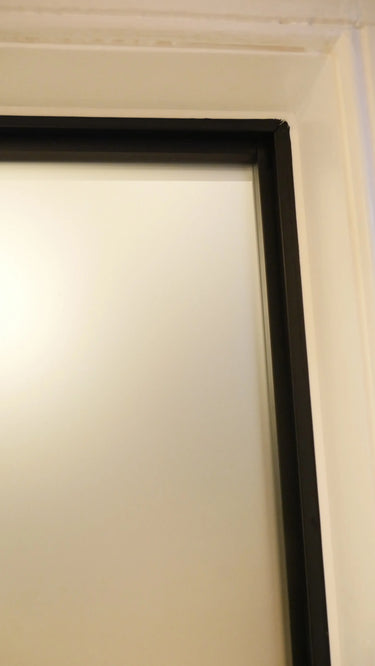 Close-up of a white hinged door with a black frame and beige wall corner in a home interior