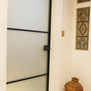Frosted glass hinged door with black frame in a white wall hallway, stained glass panels, shoes on floor