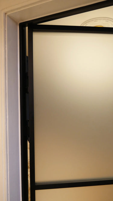Close-up of a frosted glass hinged door with black metal frame inside a beige wall frame