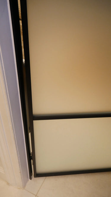 Close-up of hinged frosted glass door with black metal frame in interior setting