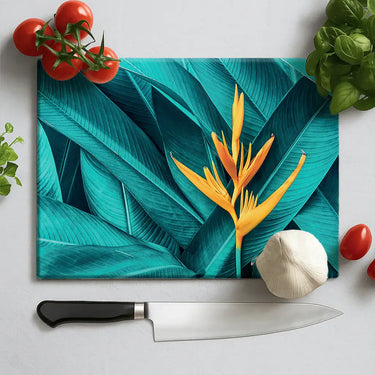 Tropical leaf design cutting board with yellow bird of paradise flower, garlic, tomatoes, basil, and chef knife
