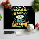 Black chopping board with colorful text 'Wake Up Be Awesome' surrounded by tomatoes, garlic, basil, and a kitchen knife