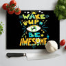 Black chopping board with colorful text 'Wake Up Be Awesome' surrounded by tomatoes, garlic, basil, and a kitchen knife