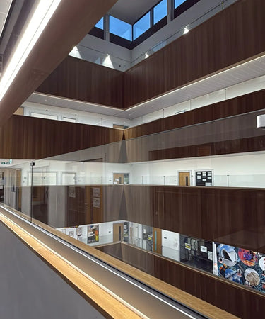 An interior architectural view of a modern multi-level atrium with dark wood paneling, glass railings, and bright ceiling lights.