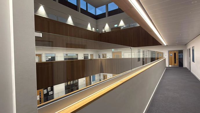A modern multi-story office building interior with a long corridor on the right, glass railings, wood paneling, and skylights above.