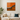Modern living room with white sofa, beige and dark green pillows, potted plant, and abstract orange wall art